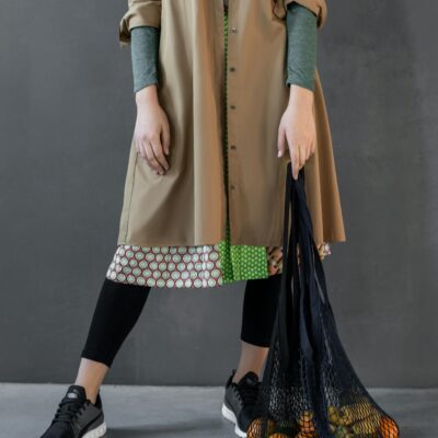 A stylish outfit featuring a trench coat and sneakers with a reusable net bag and fruits.
